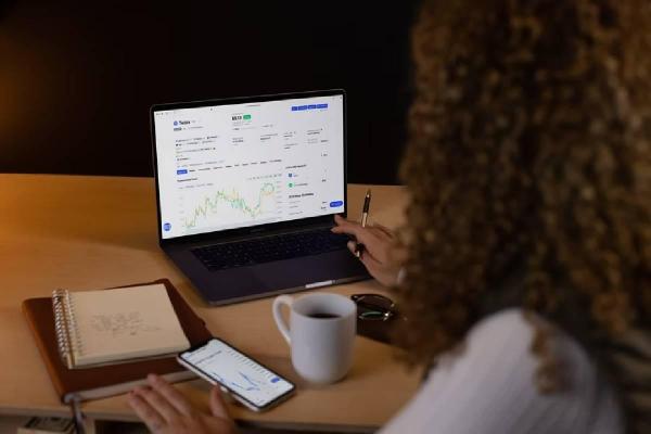 Una chica analiza el mercado en su computadora y compara con su celular. 