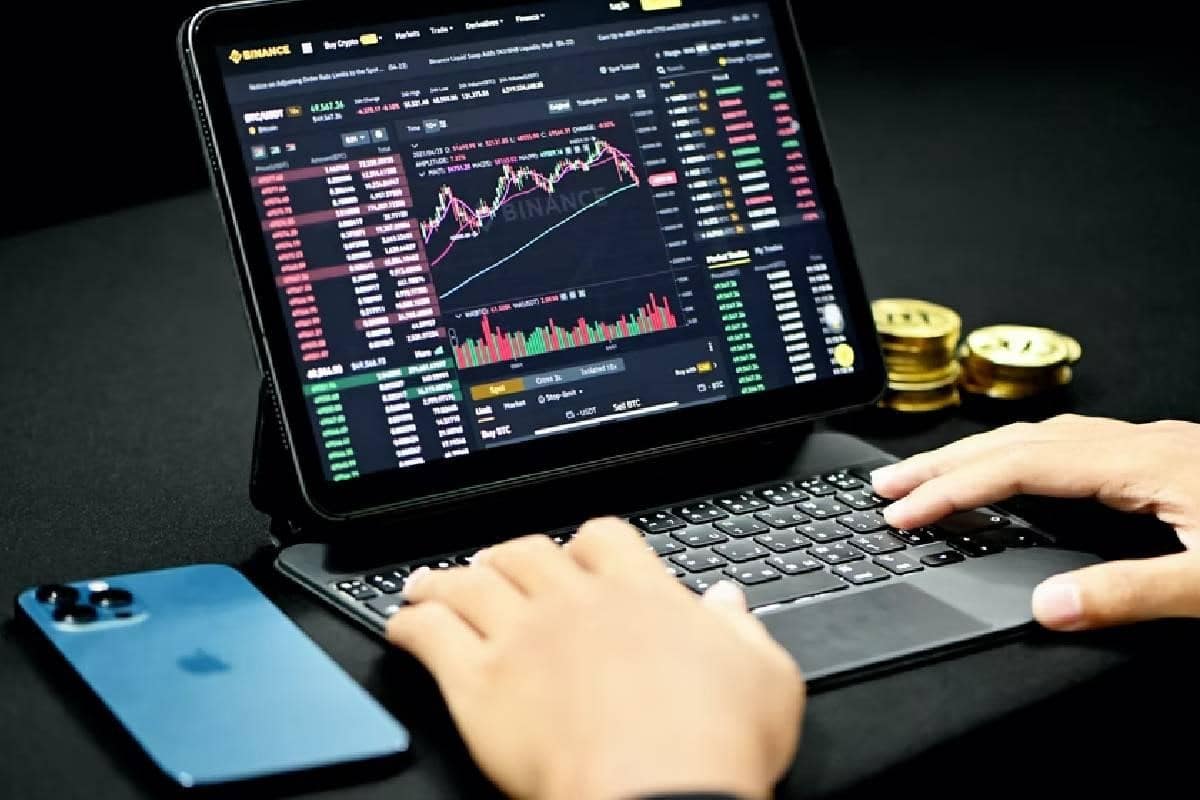 Se ven dos manos sobre una laptop en donde se ven gráficos y números relativos a las Criptomonedas.