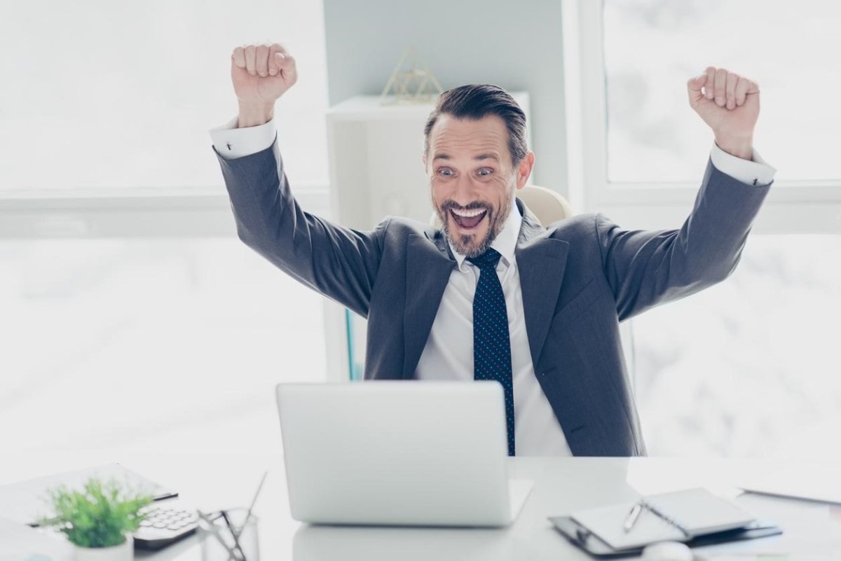 Hombre de negocios celebra frente a su computador tras descubrir qué es chat GPT.