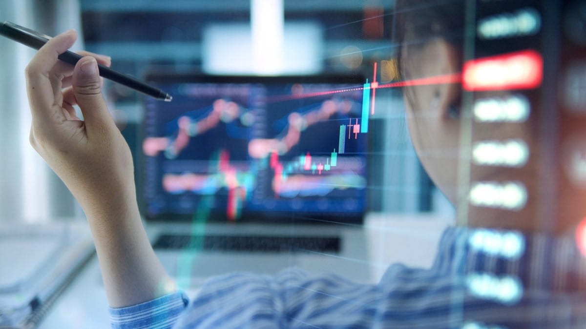 Inversionista sostiene lapicero mientras observa gráficas y amplia estrategias de trading cuantitativo.