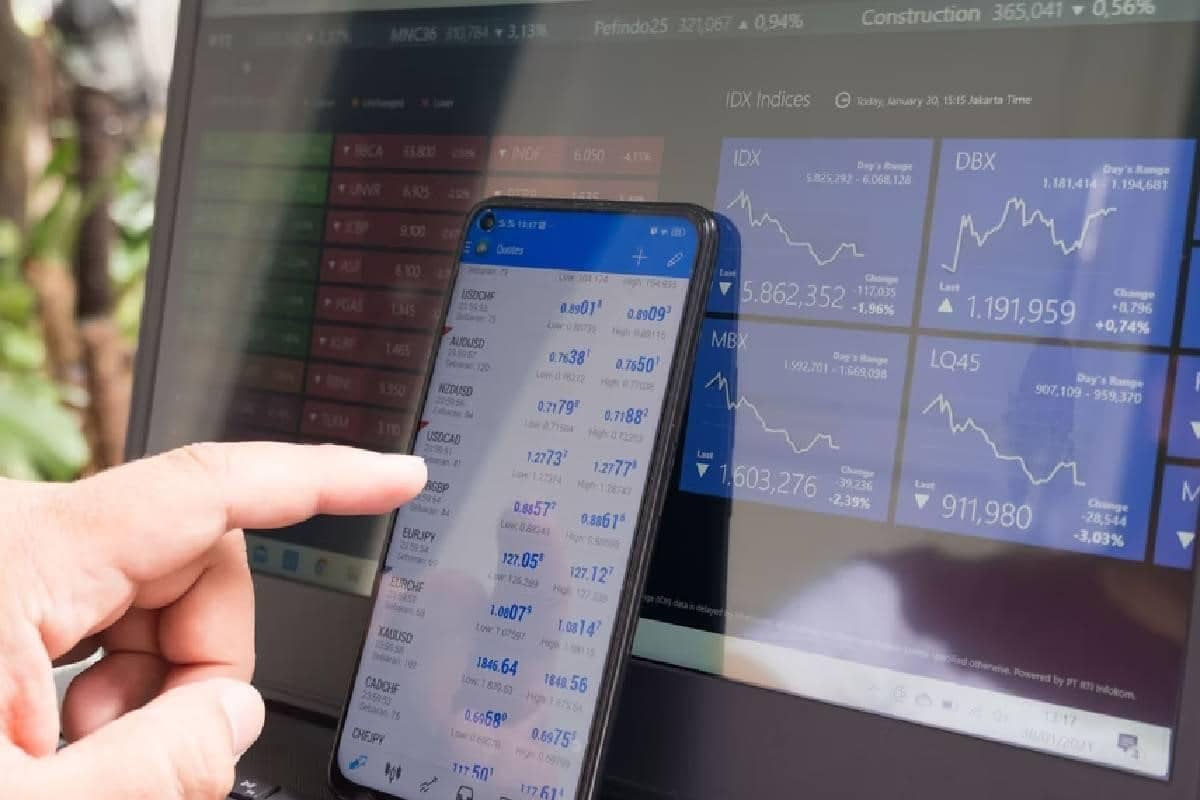 Una persona observando en su laptop y celular gráficas de trading.