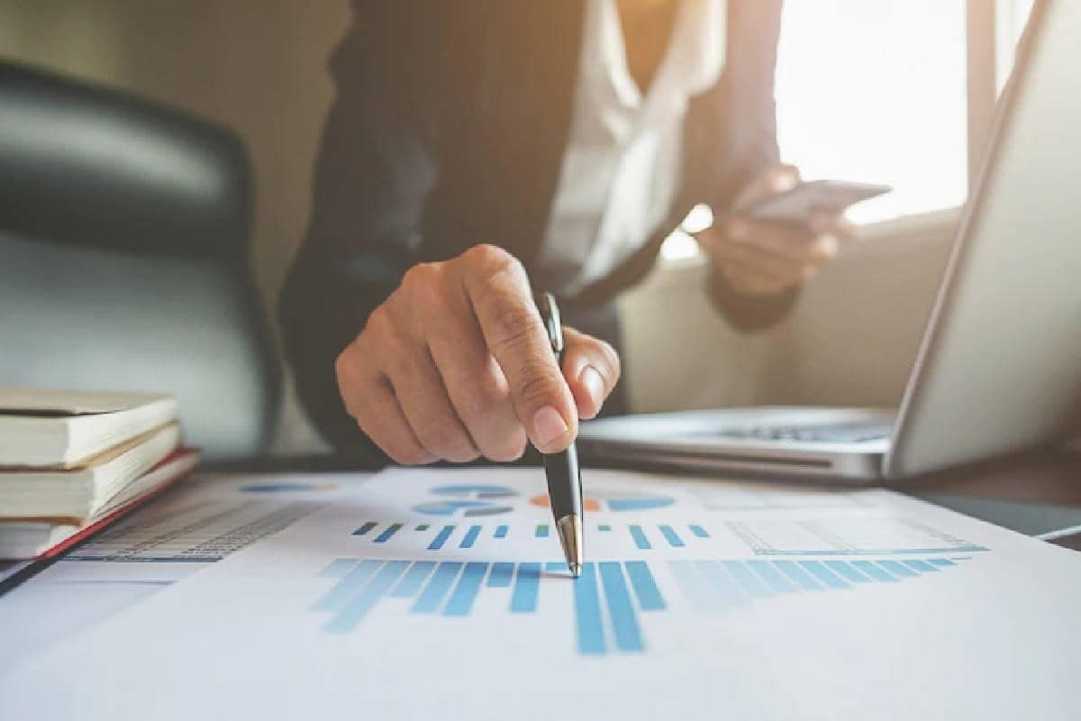 Un inversor hace cálculos en una hoja de gráficos y con su celular en la mano.