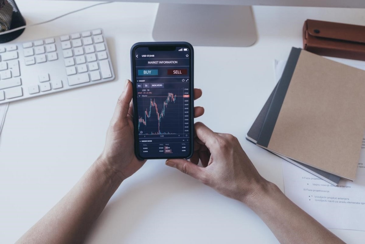 Una persona sostiene su celular mientras analiza gráficos para definir métodos de inversión.