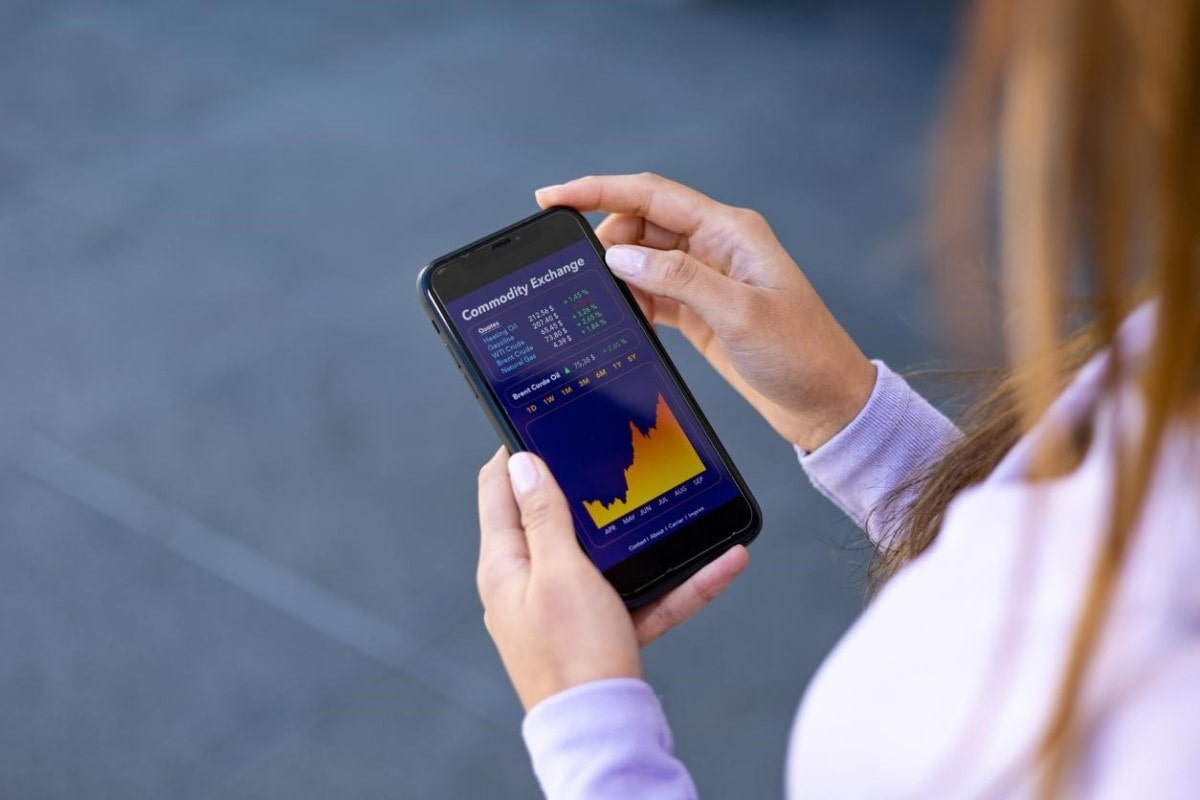 Una mujer sostiene su celular donde observa gráficos de lo que son los CFD que opera.