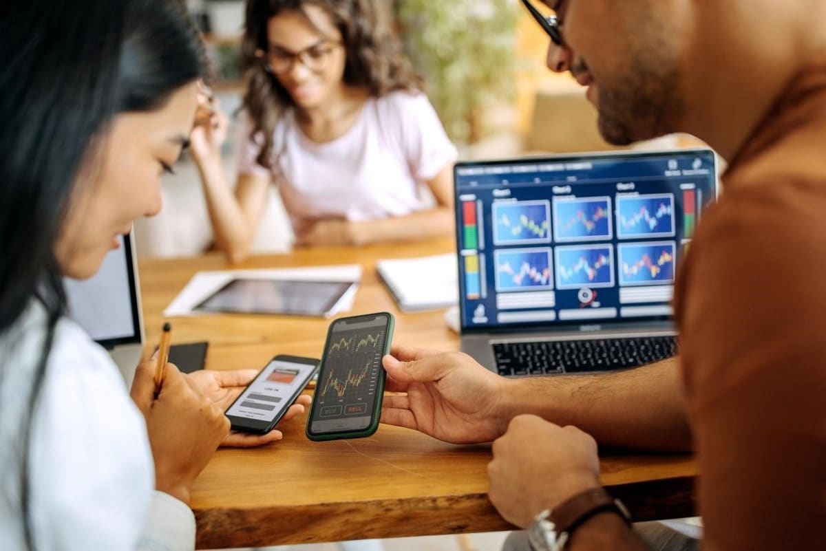 Dos jóvenes analizan en sus celulares gráficas de trading y criptomonedas.