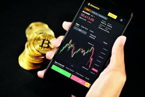 Monedas doradas que representan a las Bitcoins y un celular con gráficos de análisis financiero.