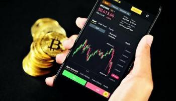 Monedas doradas que representan a las Bitcoins y un celular con gráficos de análisis financiero.