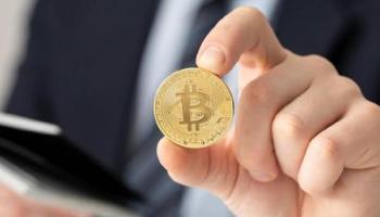 Un trader sostiene en su mano una Bitcoin.