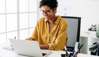 Mujer sonríe frente a su laptop tras descubrir las ventajas de una cuenta demo trading.